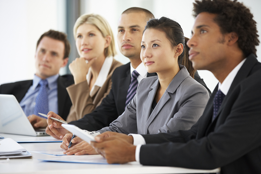 Group Of Business People Listening To Colleague Addressing Office Meeting